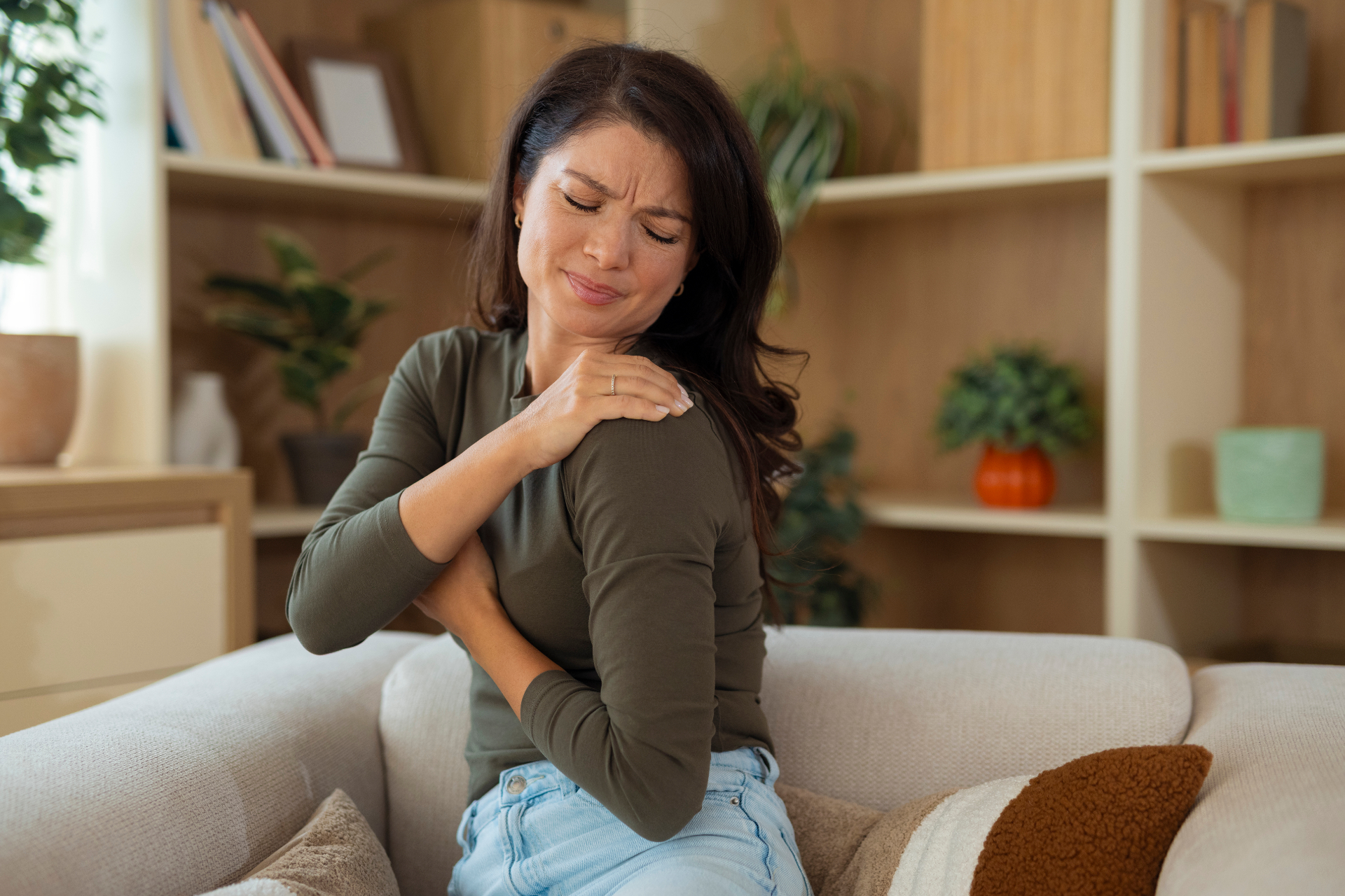 Woman in midlife holding her painful shoulder while seated at home