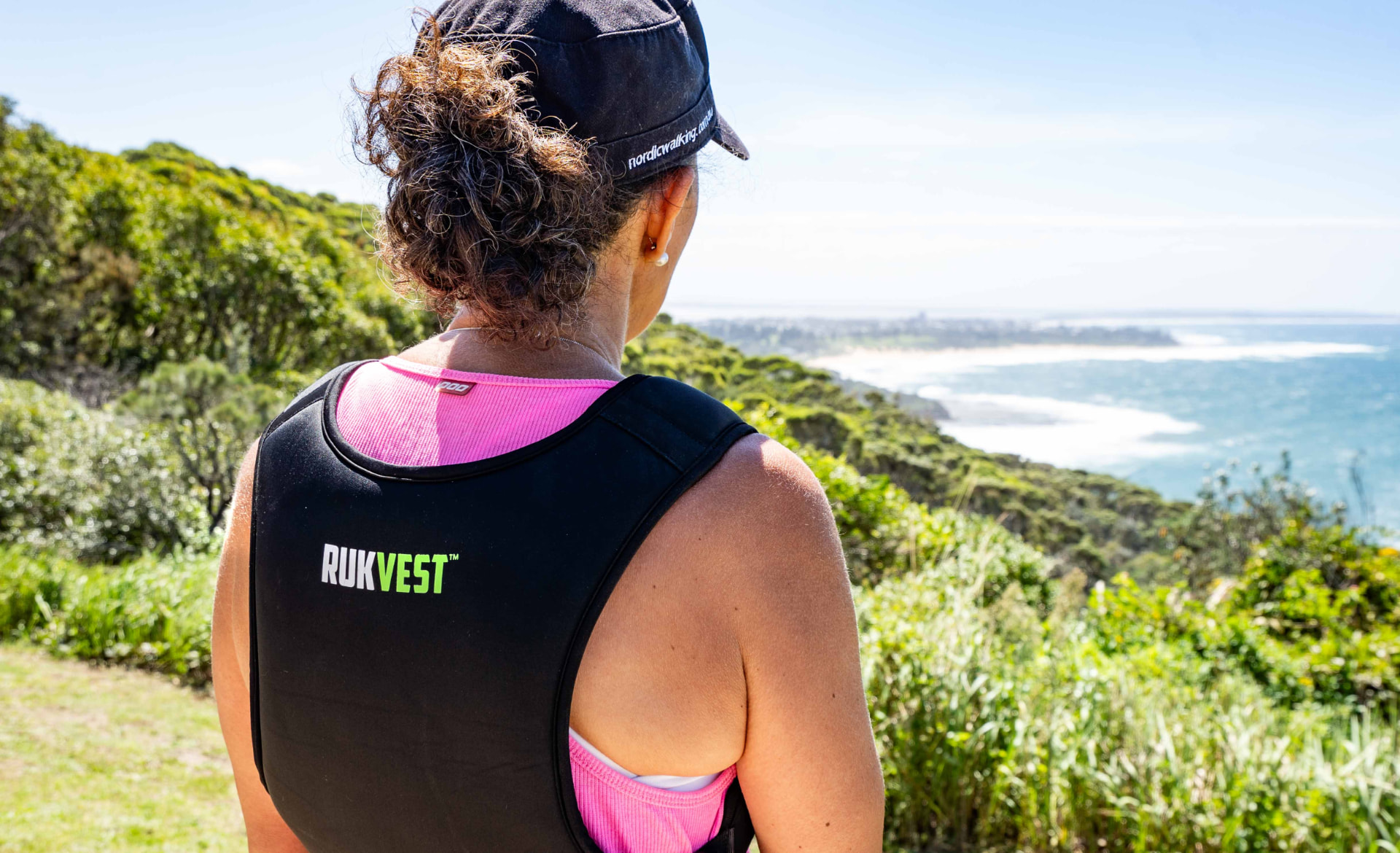 Woman wearing a RUKVEST weighted vest on a coastal bushwalk overlooking the ocean